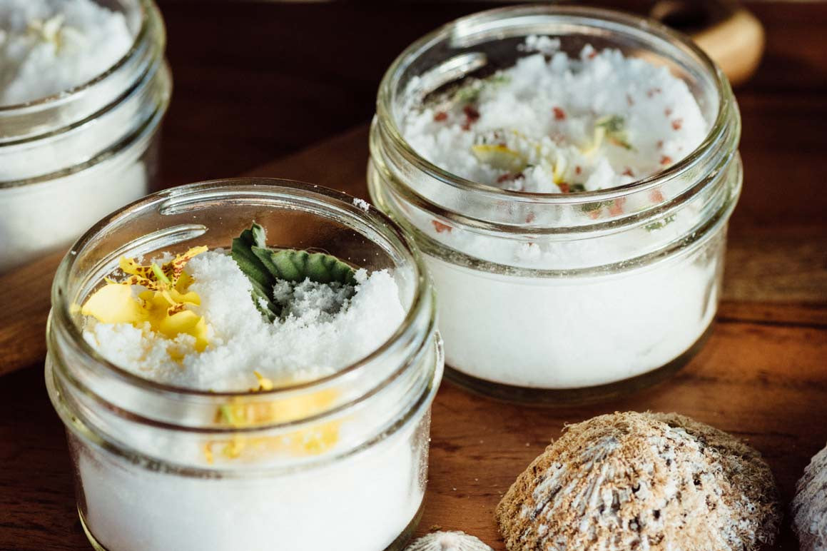 Three glass jars filled with custom bath salts on a wooden surface.
