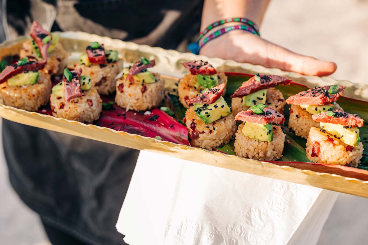 Person holding a wooden tray with assorted musubis