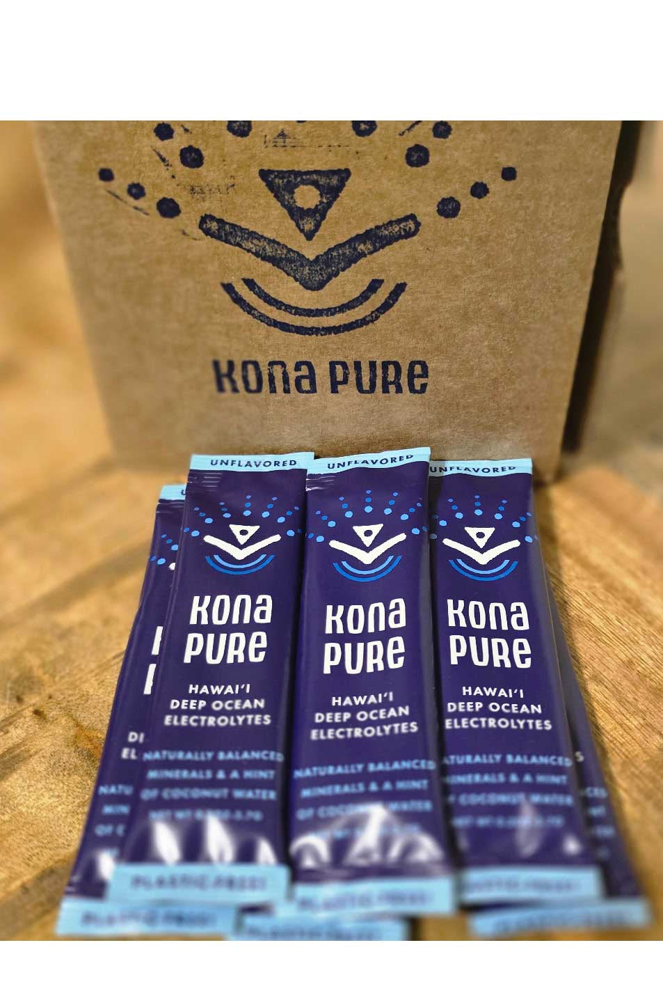 Kona Pure electrolyte packets on a wooden surface with a cardboard box in the background.