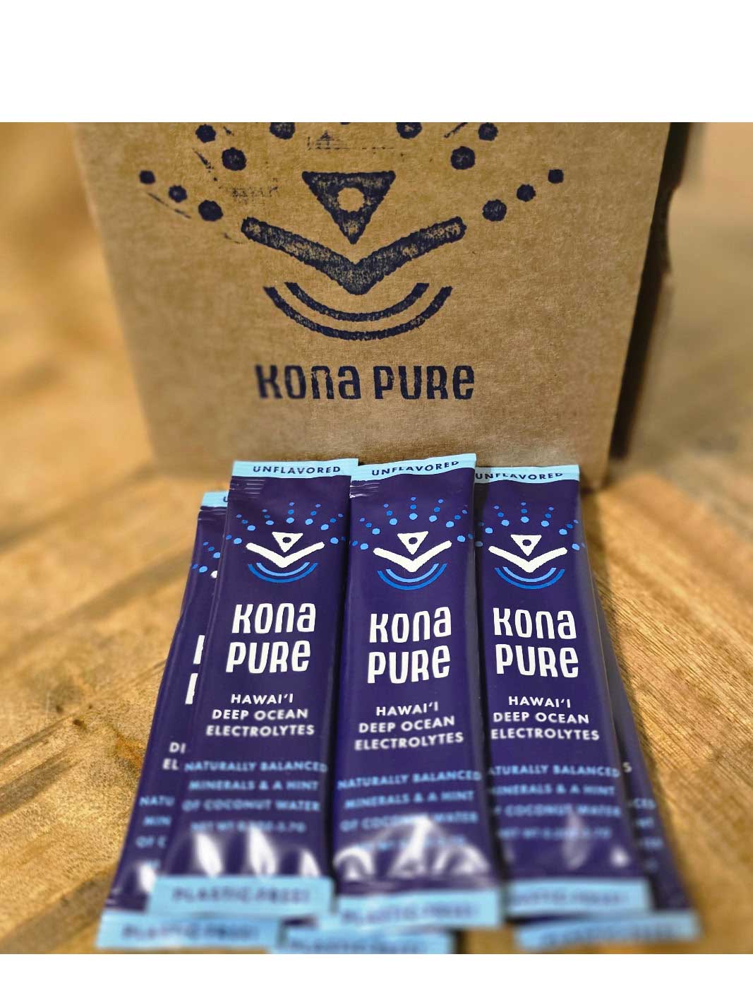 Kona Pure electrolyte packets on a wooden surface with a cardboard box in the background.