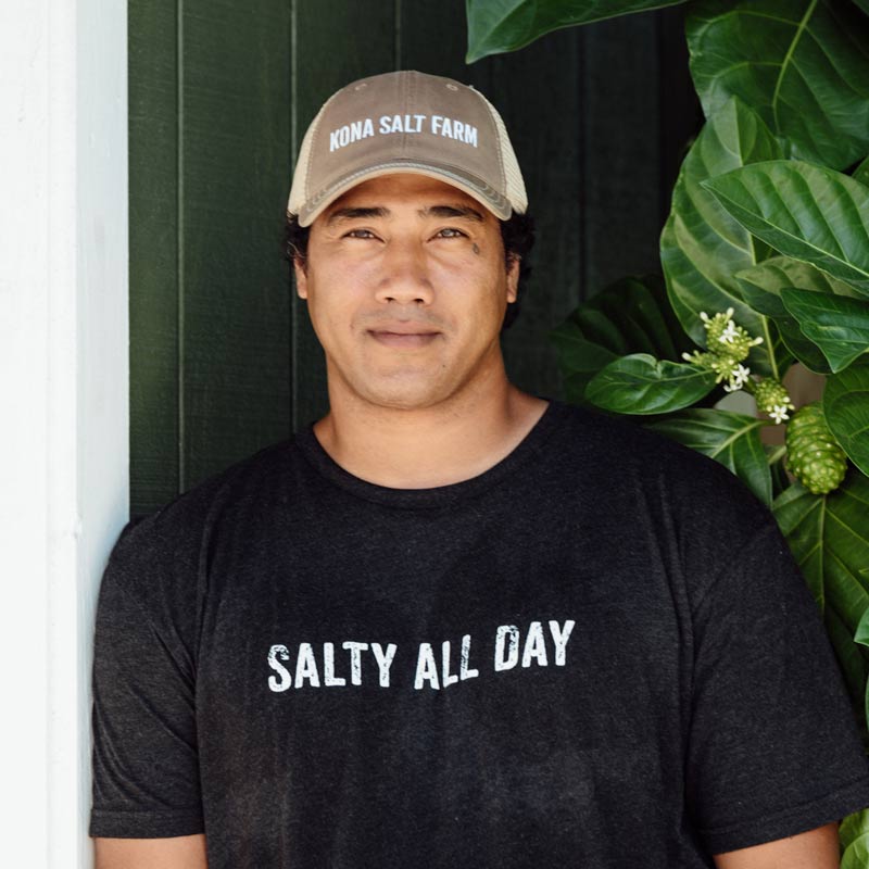 Man wearing a cap and t-shirt with 'Salty All Day' text, standing outdoors with greenery.