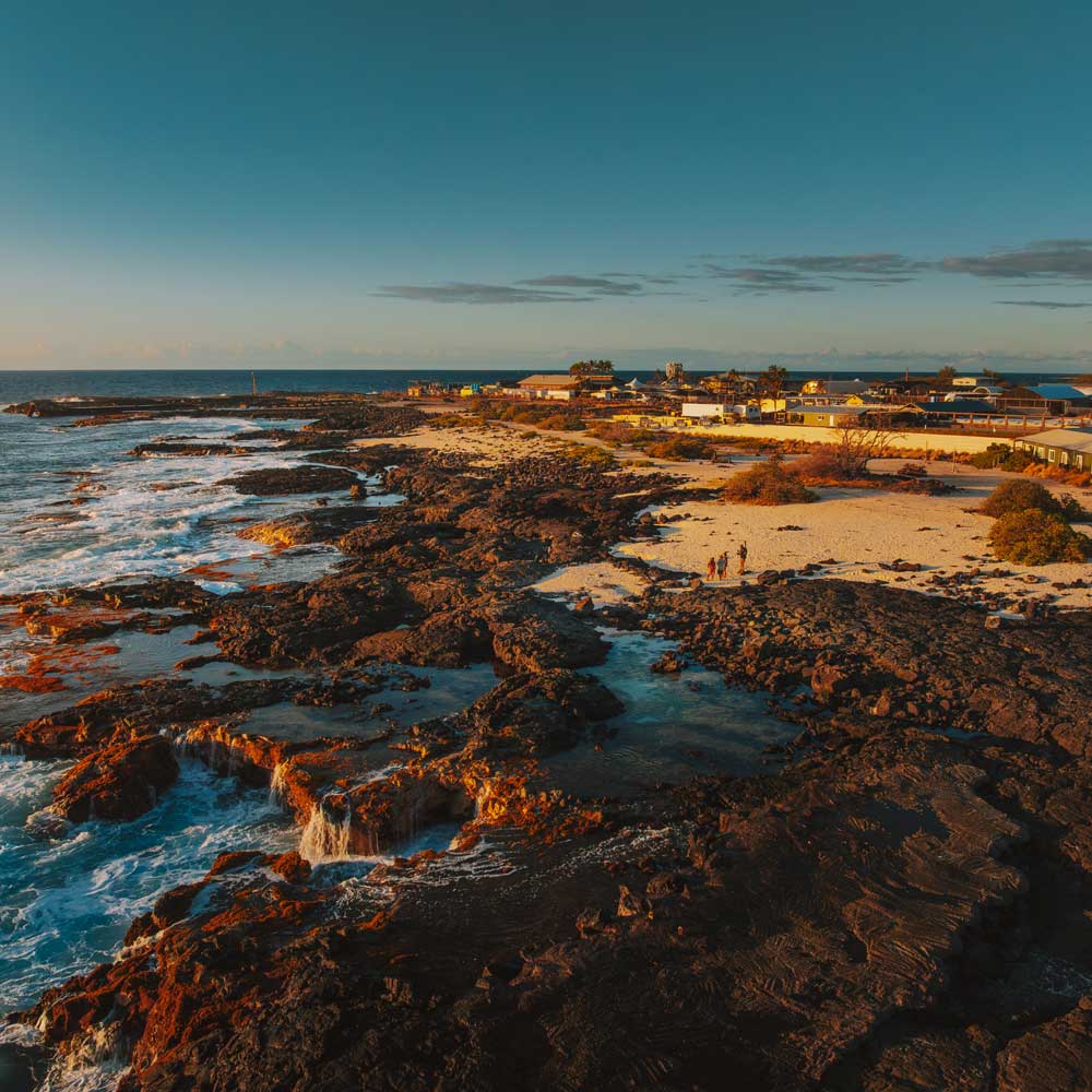 Kona coastline with rocks and beach with ocean waves at sunset