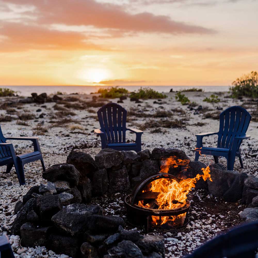 Fire pit with blue chairs around it during sunset at the Kona Salt Farm.
