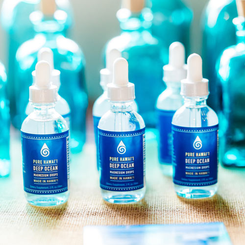 Bottles of Pure Hawaii Deep Ocean Magnesium Drops on a textured surface with blurred background