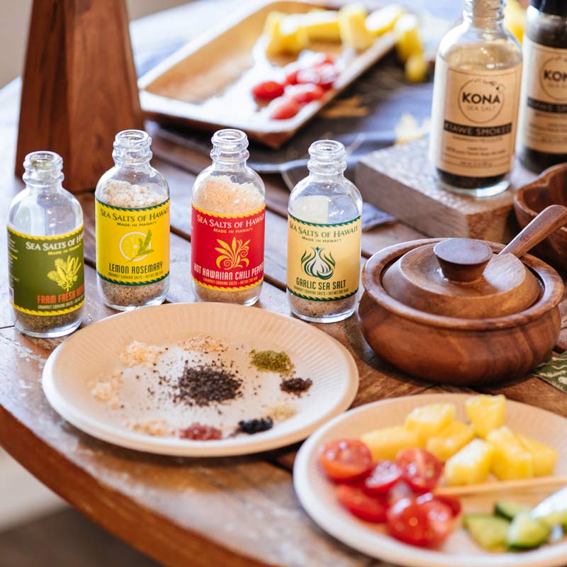 Assorted sea salt bottles on a table with assorted fruits and vegetables for tasting.